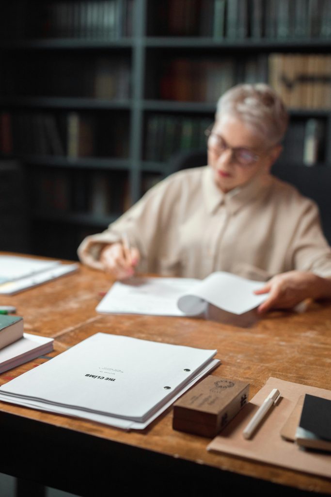 An editor is focused on reviewing and editing manuscripts at a wooden office table filled with papers.